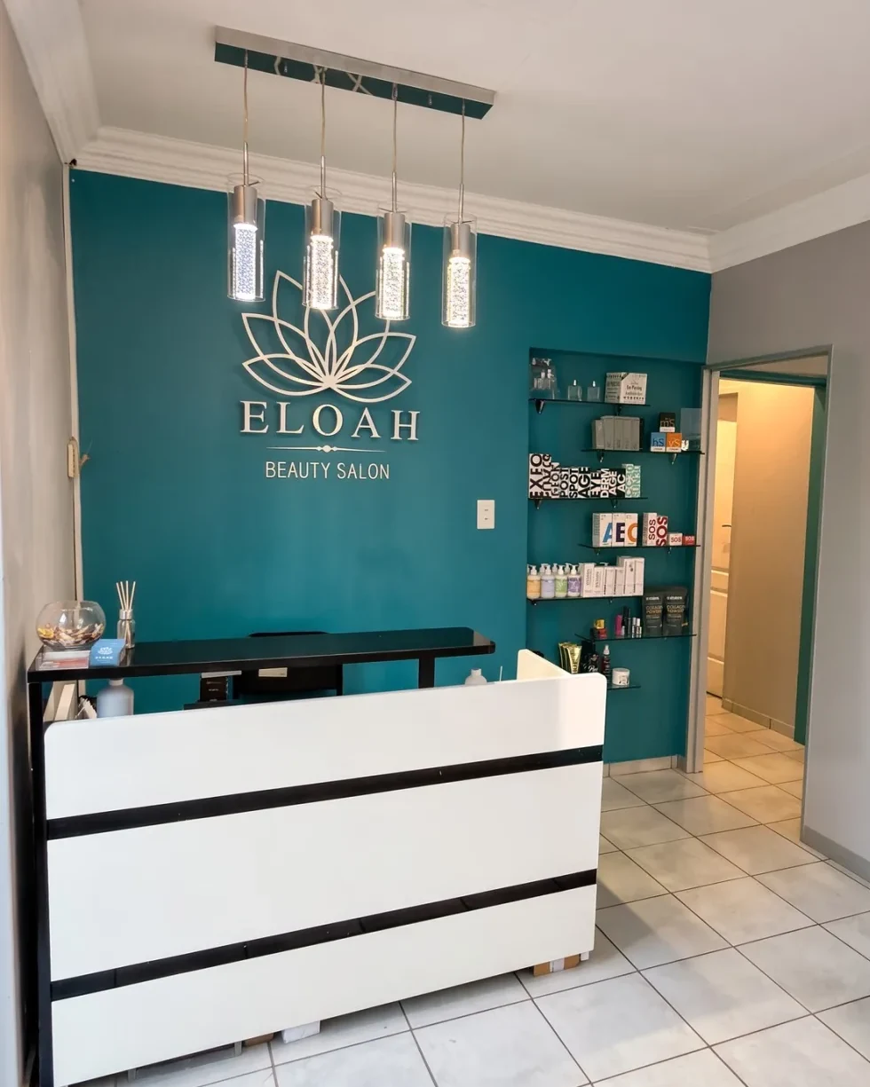 The reception desk of Eloah, a beauty salon in Centurion, in front of the teal wall with the silver ELOAH lotus sign
