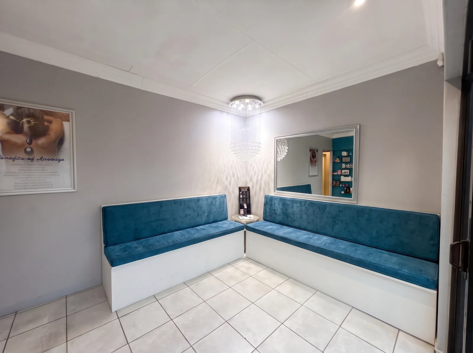 The Eloah waiting area with white benches dressed in blue seat and back cushions under a crystal chandelier